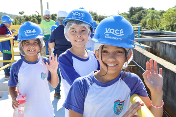 Crianças sorrindo e usando capacetes azuis durante uma atividade educativa.